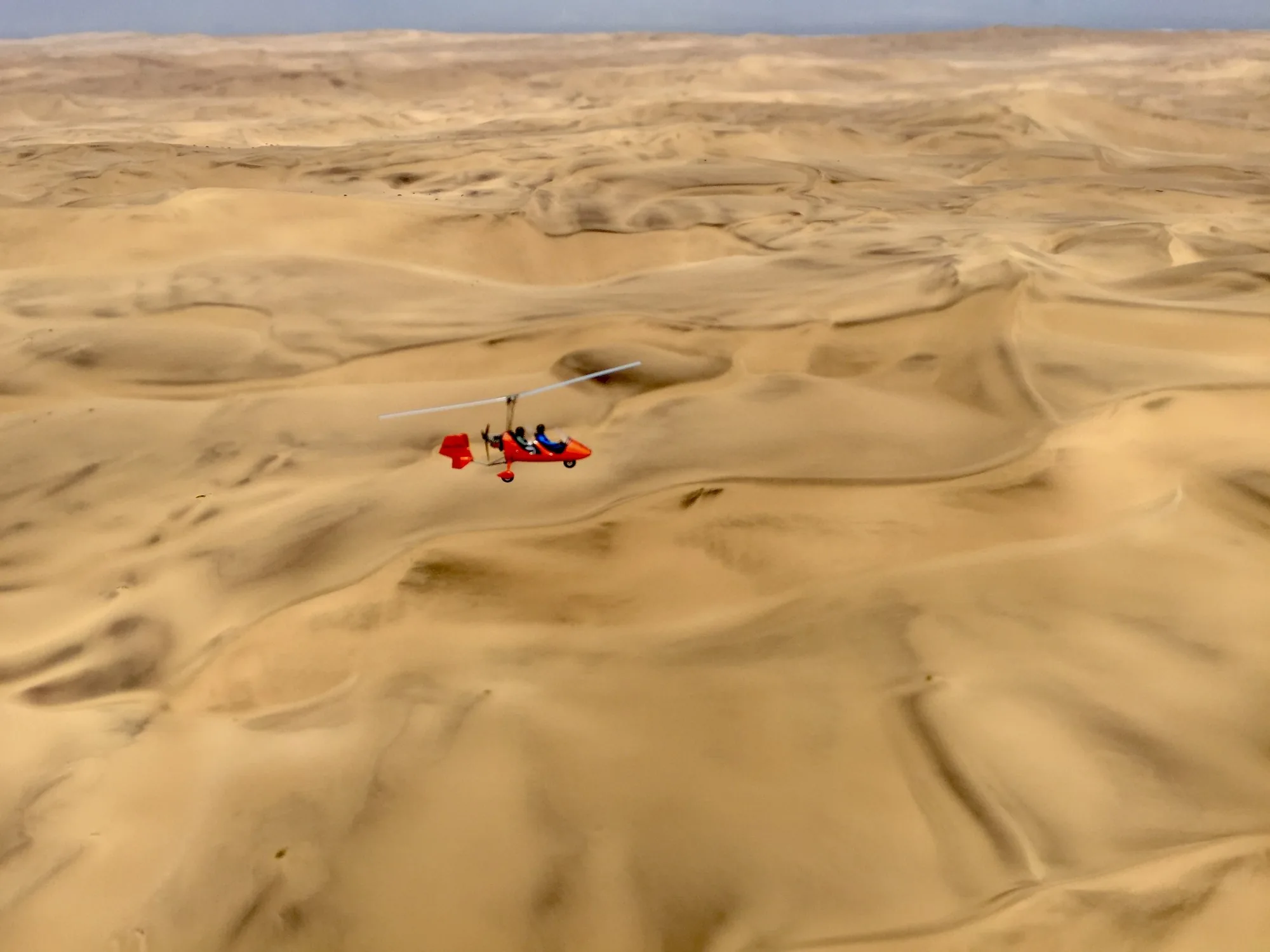 Red gyroplane flying above the Namib dunes